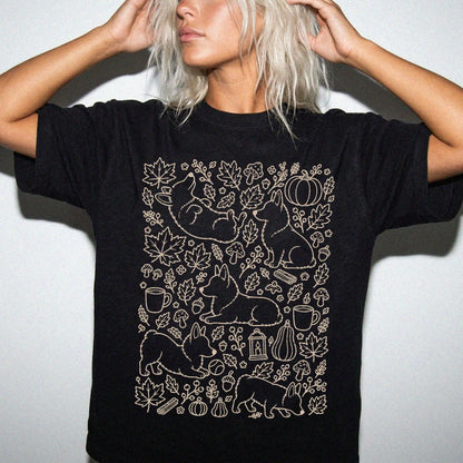 Model wearing a Black Comfort Colors® T-shirt with Corgi dogs with pumpkins, leaves, acorns, and woodland details