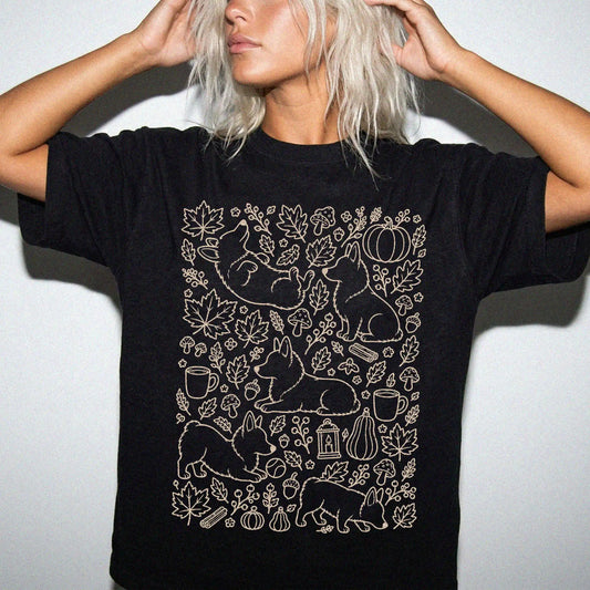 Model wearing a Black Comfort Colors® T-shirt with Corgi dogs with pumpkins, leaves, acorns, and woodland details