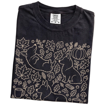 Folded Black Comfort Colors® T-shirt showing Corgi dogs with pumpkins, leaves, acorns, and woodland details