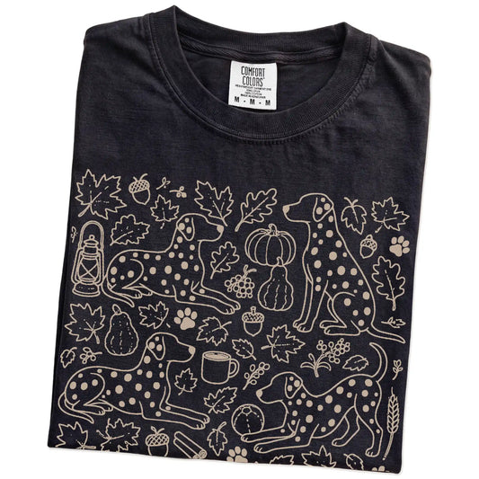 Folded Black Comfort Colors® T-shirt showing Dalmatian dogs with pumpkins, leaves, acorns, and woodland details
