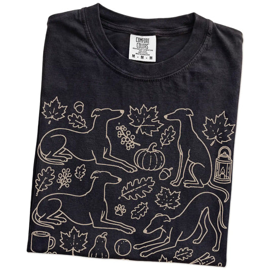 Folded Black Comfort Colors® T-shirt showing Greyhound dogs with pumpkins, leaves, acorns, and woodland details