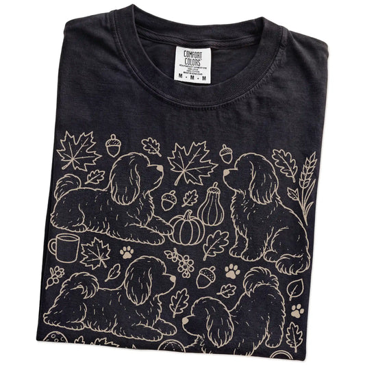 Folded Black Comfort Colors® T-shirt showing Havanese dogs with pumpkins, leaves, acorns, and woodland details