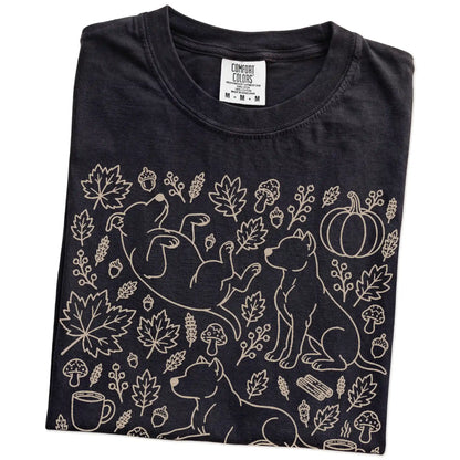 Folded Black Comfort Colors® T-shirt showing Pitbull dogs with pumpkins, leaves, acorns, and woodland details