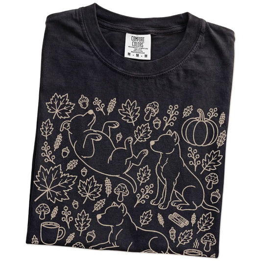 Folded Black Comfort Colors® T-shirt showing Pitbull dogs with pumpkins, leaves, acorns, and woodland details