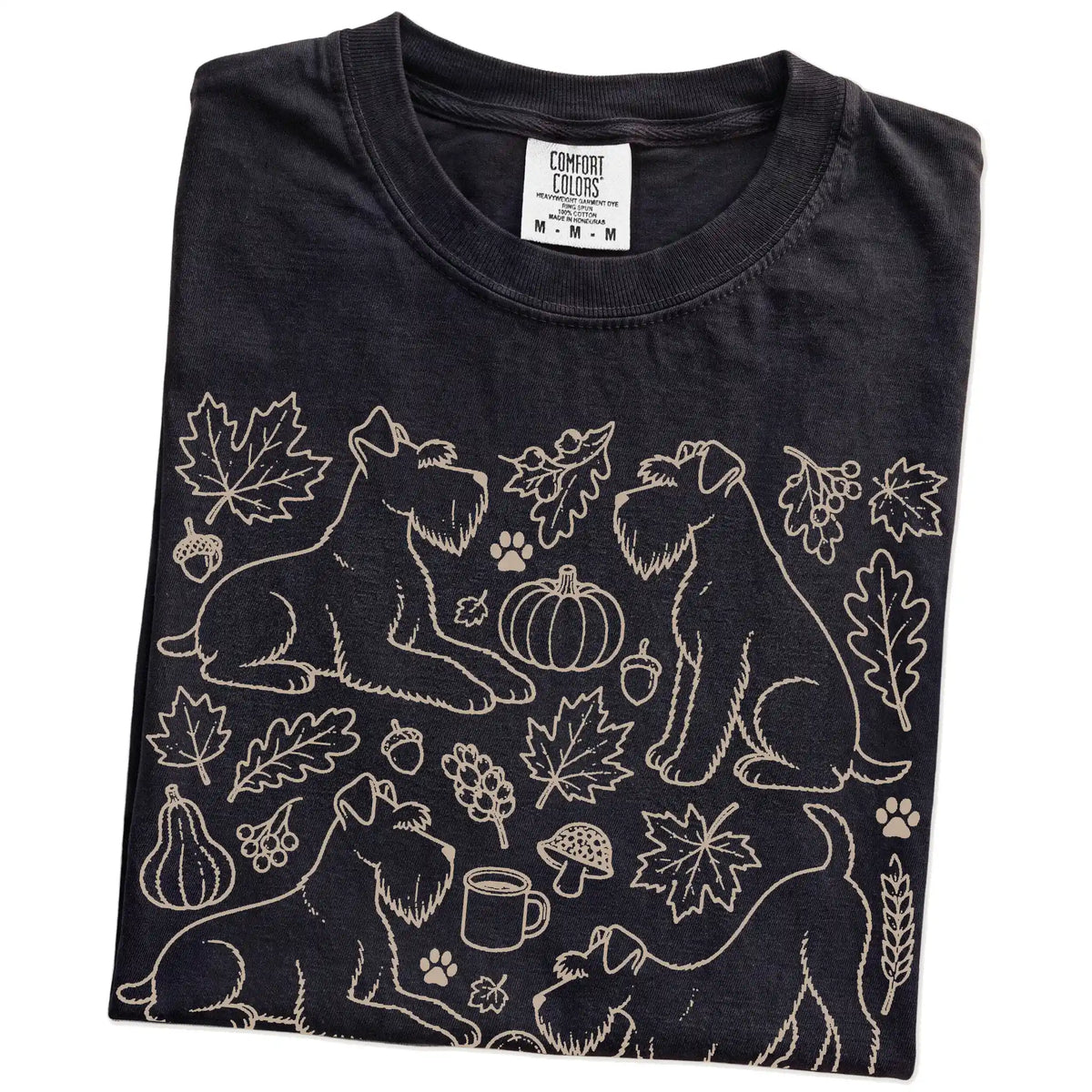 Folded Black Comfort Colors® T-shirt showing Schnauzer dogs with pumpkins, leaves, acorns, and woodland details