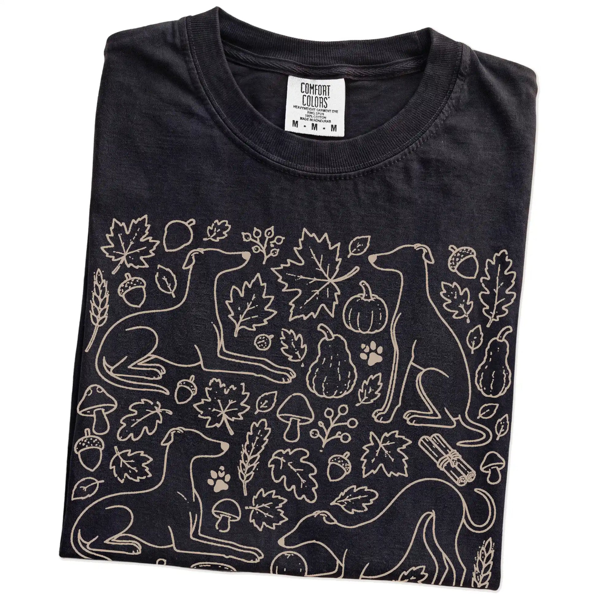 Folded Black Comfort Colors® T-shirt showing Whippet dogs with pumpkins, leaves, acorns, and woodland details