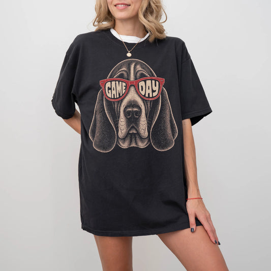 Model wearing a Black Comfort Colors® T-shirt with basset hound wearing red game day sunglasses
