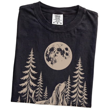 Folded Black Comfort Colors® T-shirt showing a Basset Hound howling beneath the moon and pine trees
