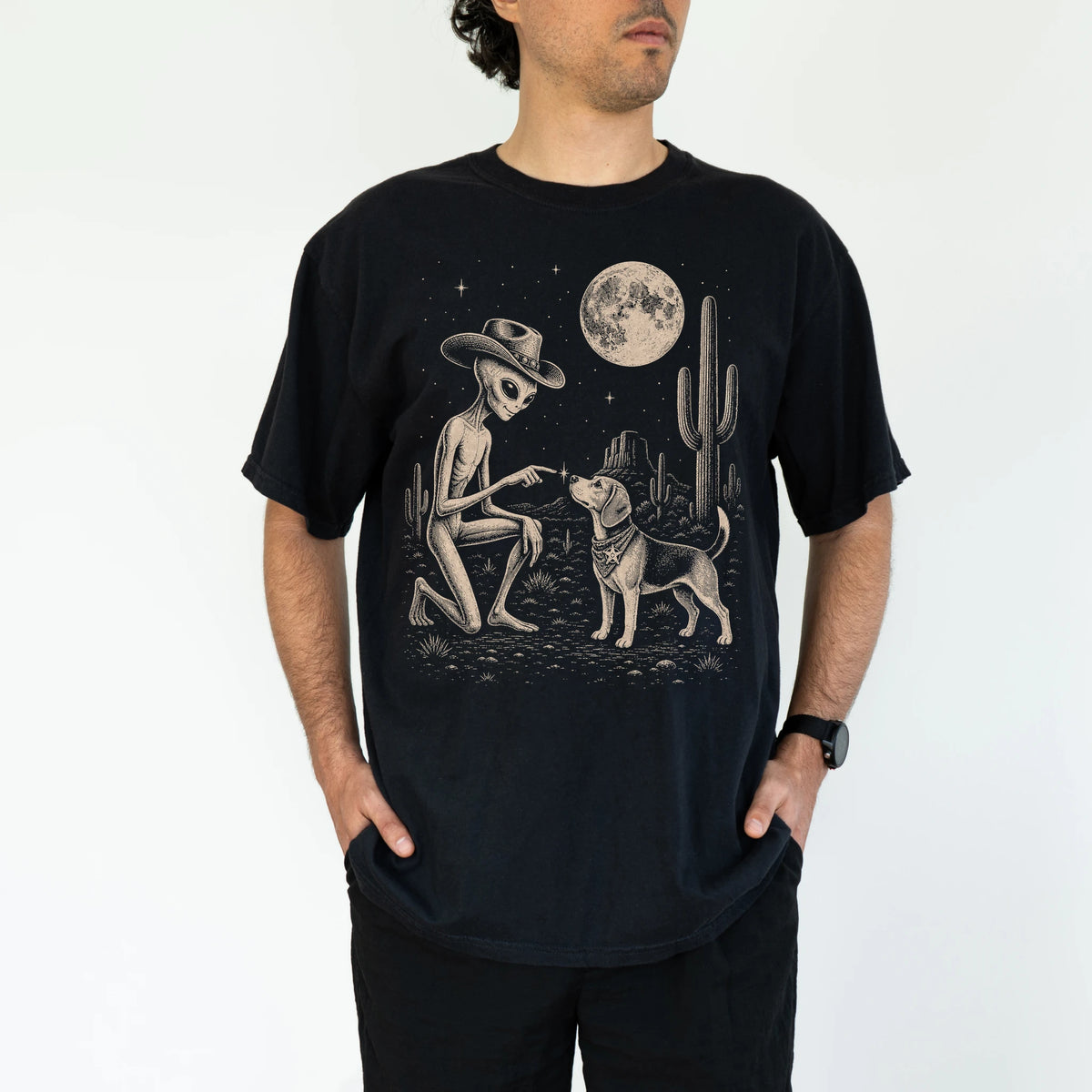 Model wearing a Black Comfort Colors® T-shirt with cowboy alien fist-bumping a beagle beneath the moon