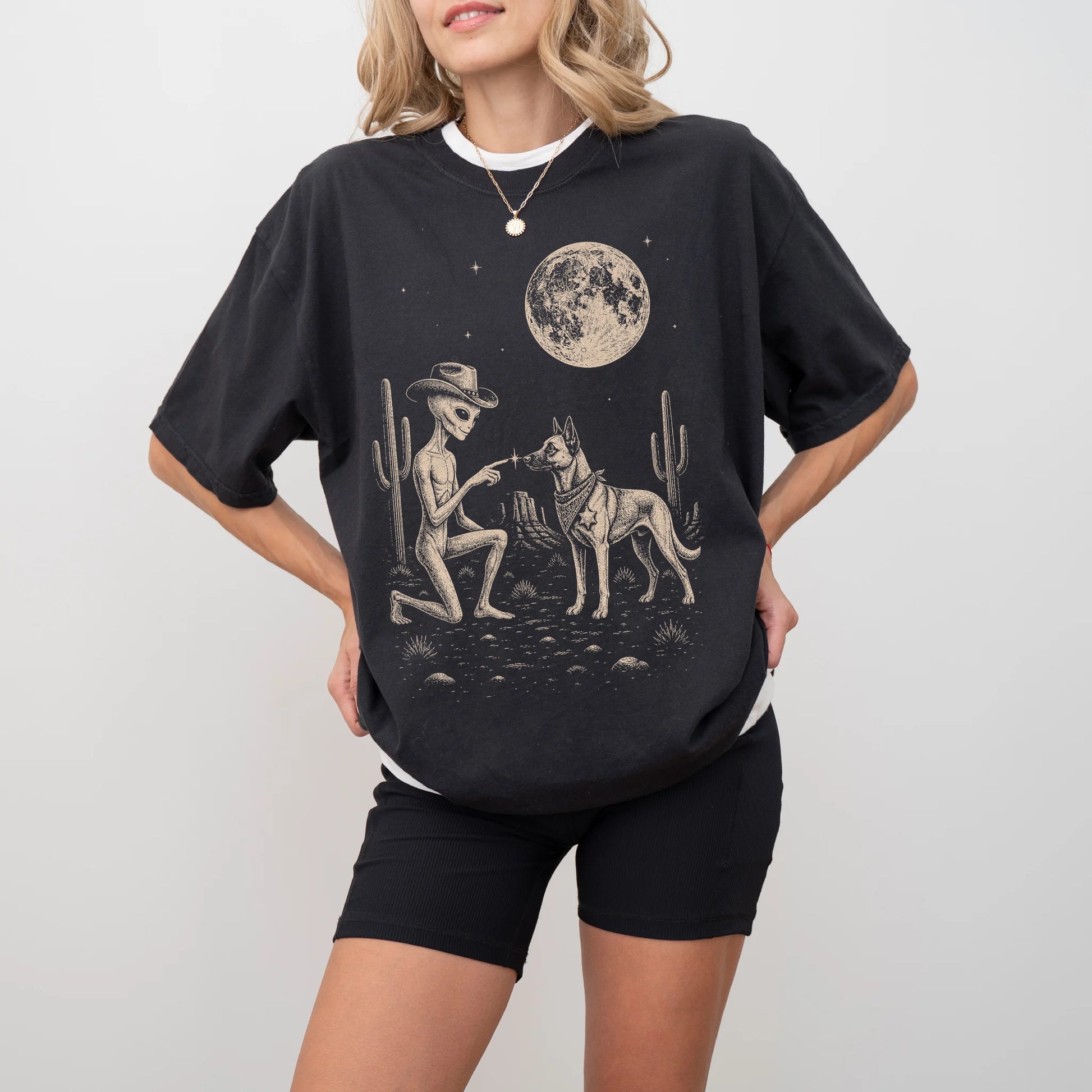 Model wearing a Black Comfort Colors® T-shirt with cowboy alien fist-bumping a belgian malinois beneath the moon