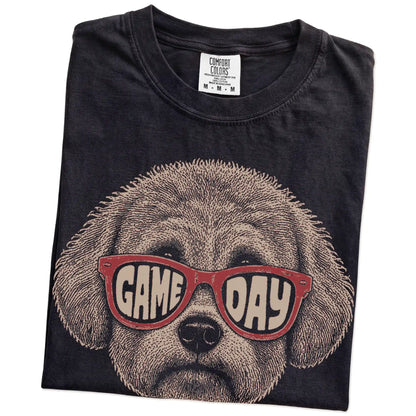 Folded Black Comfort Colors® T-shirt showing bichon frise wearing red game day sunglasses