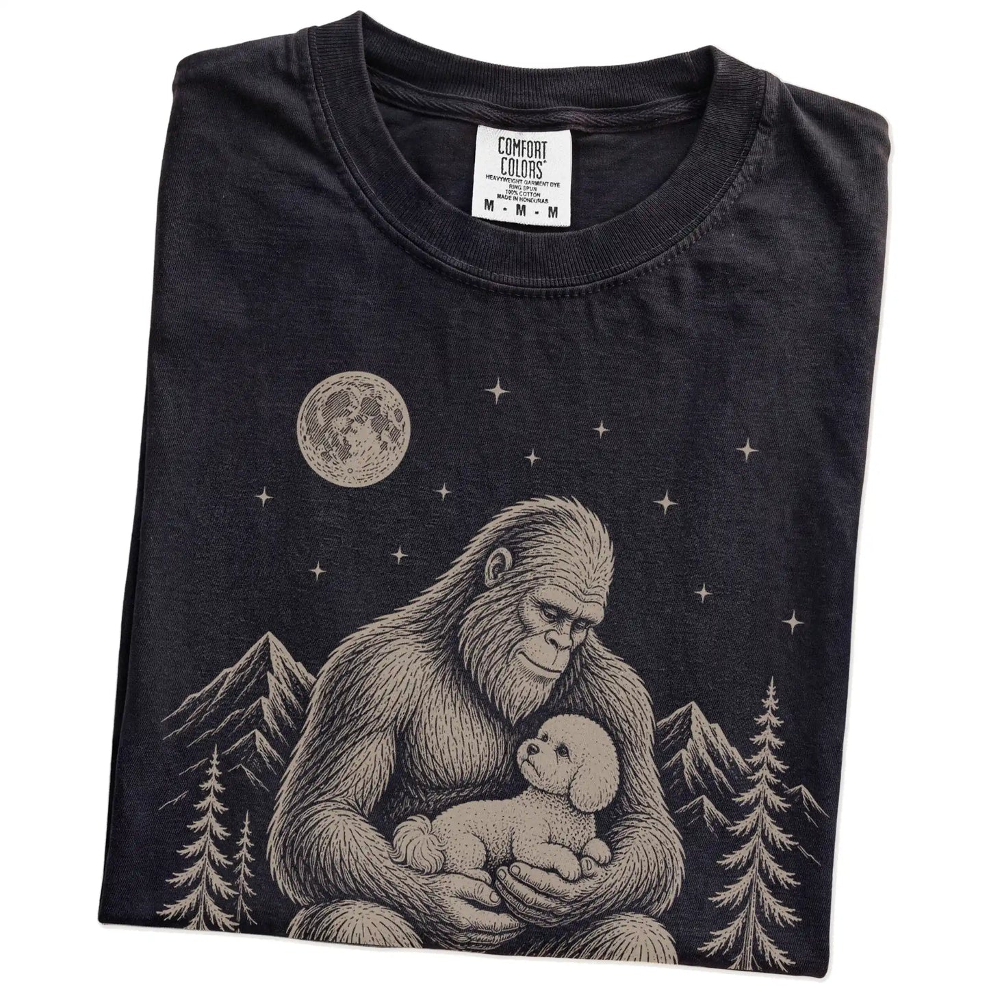 Folded Black Comfort Colors® T-shirt showing Bigfoot holding a Bichon Frise