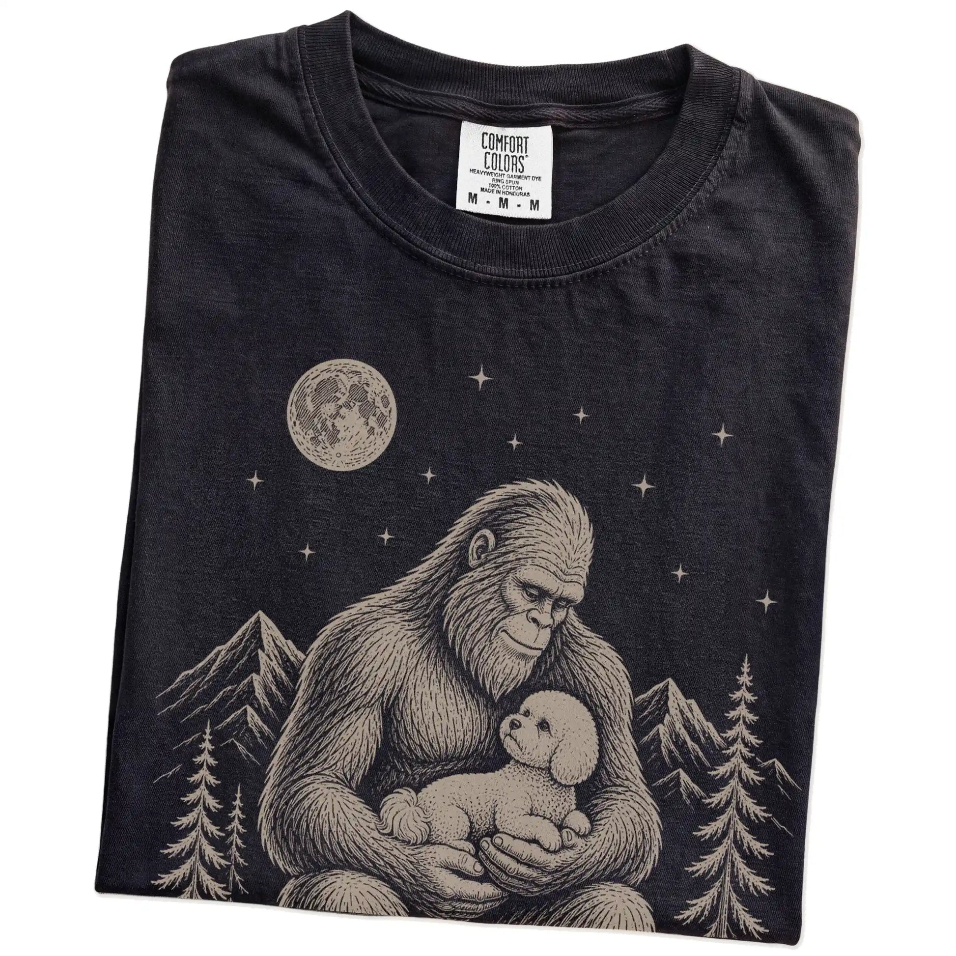 Folded Black Comfort Colors® T-shirt showing Bigfoot holding a Bichon Frise