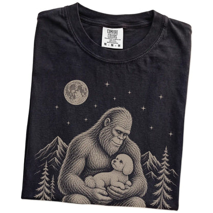 Folded Black Comfort Colors® T-shirt showing Bigfoot holding a Bichon Frise
