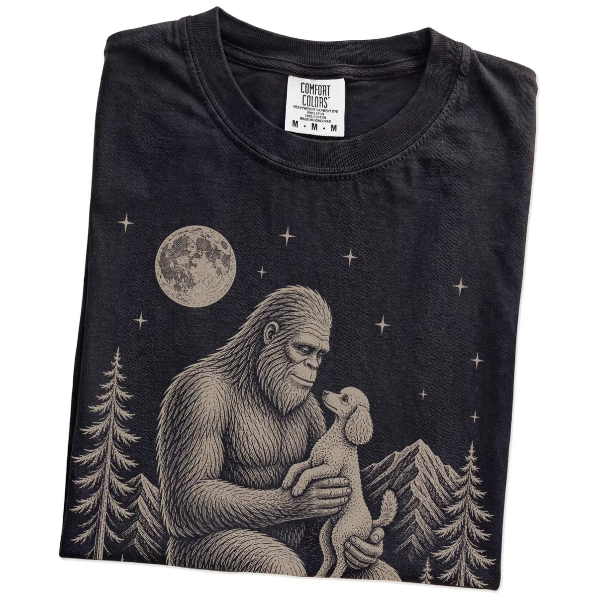 Folded Black Comfort Colors® T-shirt showing Bigfoot holding a Poodle (Miniature)