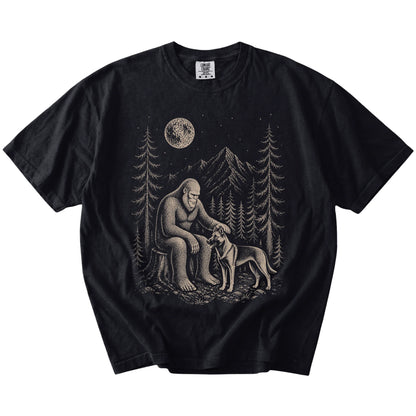 Bigfoot petting a Belgian Malinois beneath the moon in a pine forest on a Black Comfort Colors® T-shirt
