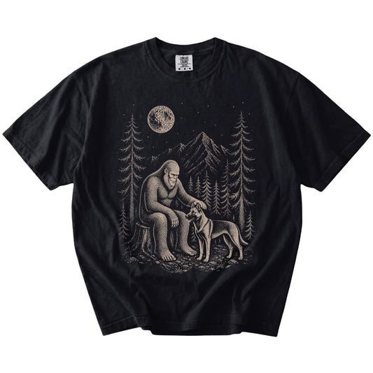 Bigfoot petting a Belgian Malinois beneath the moon in a pine forest on a Black Comfort Colors® T-shirt