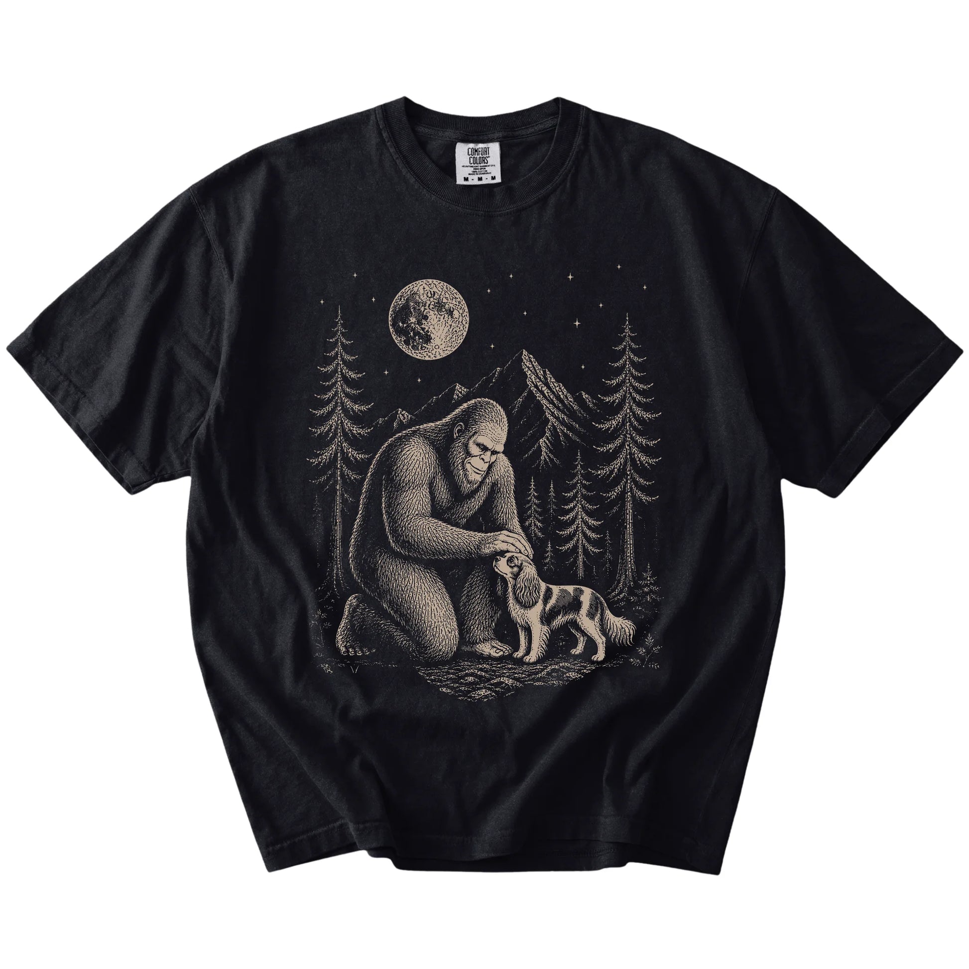 Bigfoot petting a Cavalier King Charles Spaniel beneath the moon in a pine forest on a Black Comfort Colors® T-shirt