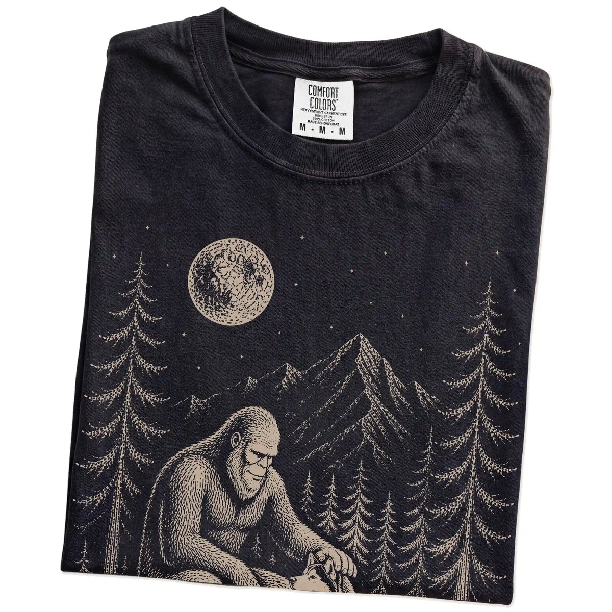 Folded Black Comfort Colors® T-shirt showing bigfoot petting a husky beneath the moon in a pine forest