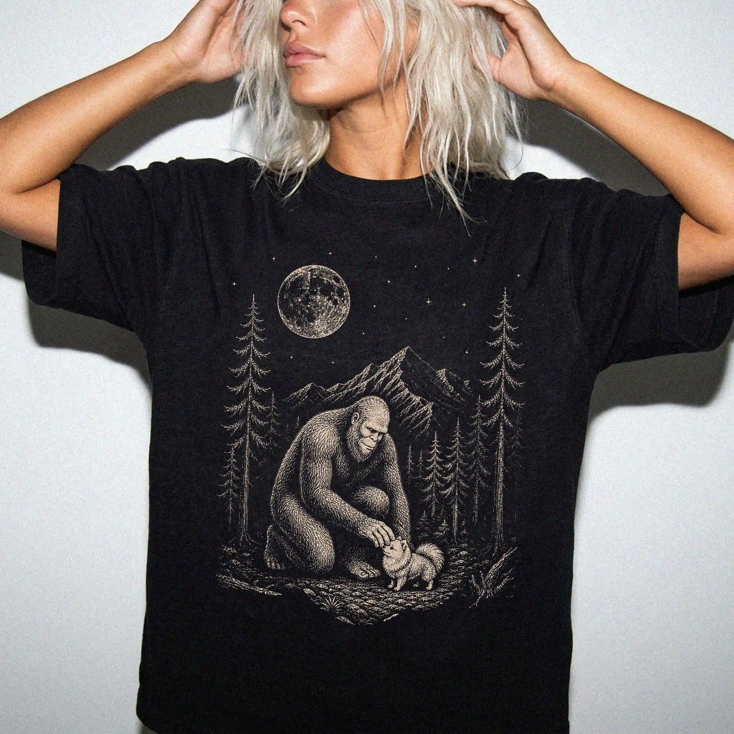 Model wearing a Black Comfort Colors® T-shirt with bigfoot petting a pomeranian beneath the moon in a pine forest