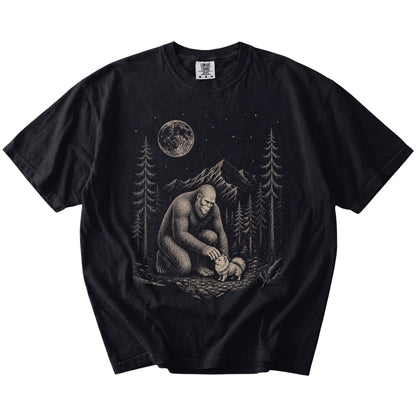 Bigfoot petting a Pomeranian beneath the moon in a pine forest on a Black Comfort Colors® T-shirt