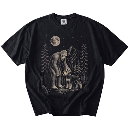 Bigfoot petting a Schnauzer beneath the moon in a pine forest on a Black Comfort Colors® T-shirt