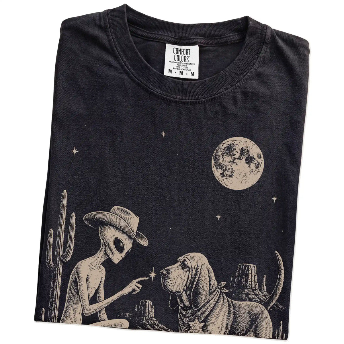 Folded Black Comfort Colors® T-shirt showing cowboy alien fist-bumping a bloodhound beneath the moon