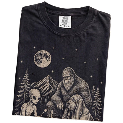 Folded Black Comfort Colors® T-shirt showing Bloodhound camping with Bigfoot and an alien