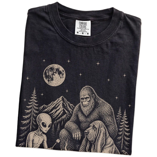 Folded Black Comfort Colors® T-shirt showing Bloodhound camping with Bigfoot and an alien