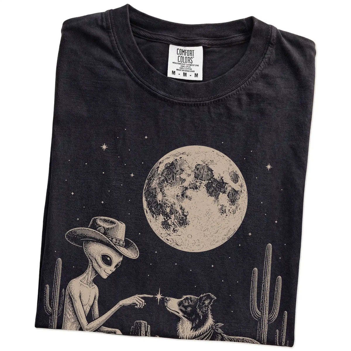 Folded Black Comfort Colors® T-shirt showing cowboy alien fist-bumping a border collie beneath the moon