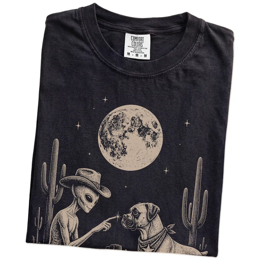 Folded Black Comfort Colors® T-shirt showing cowboy alien fist-bumping a boxer beneath the moon