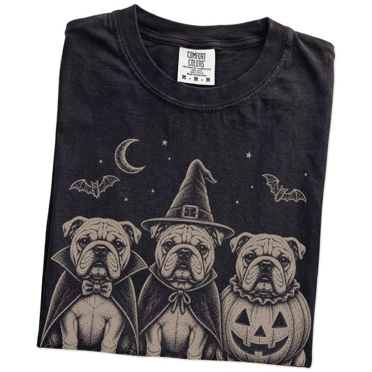Folded Black Comfort Colors® T-shirt showing three Bulldog dogs dressed for Halloween beneath bats and a crescent moon