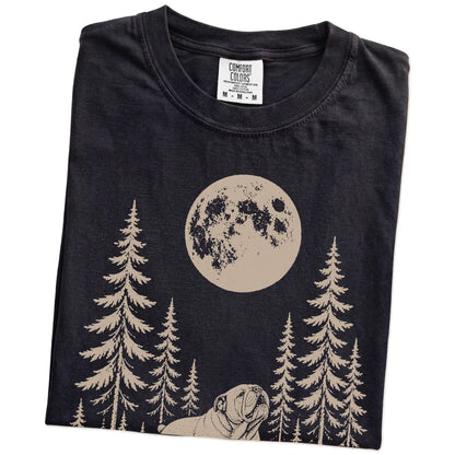 Folded Black Comfort Colors® T-shirt showing a Bulldog howling beneath the moon and pine trees