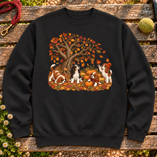 Four Cavalier King Charles Spaniel puppies with pumpkins beneath an autumn tree on a Black crewneck sweatshirt