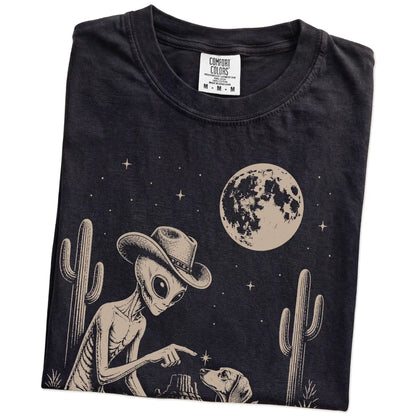 Folded Black Comfort Colors® T-shirt showing cowboy alien fist-bumping a dachshund beneath the moon