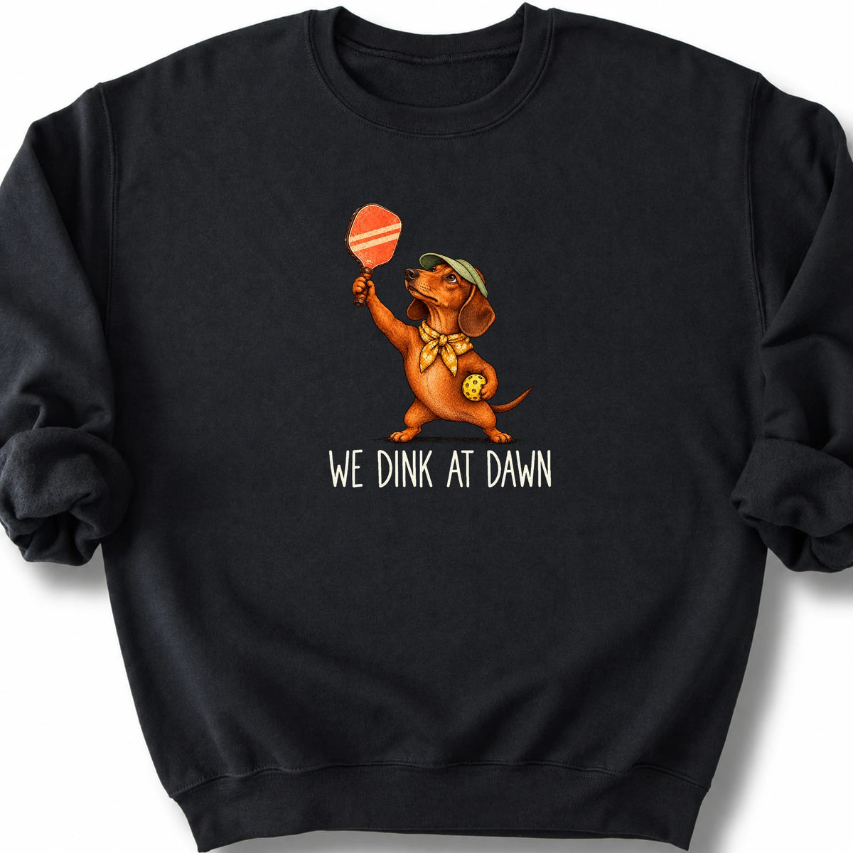 Dachshund with a pickleball paddle and ball on a Black Gildan® sweatshirt with We Dink at Dawn text