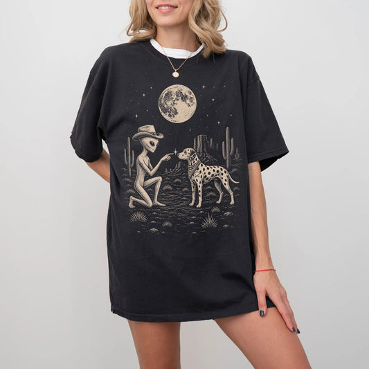 Model wearing a Black Comfort Colors® T-shirt with cowboy alien fist-bumping a dalmatian beneath the moon