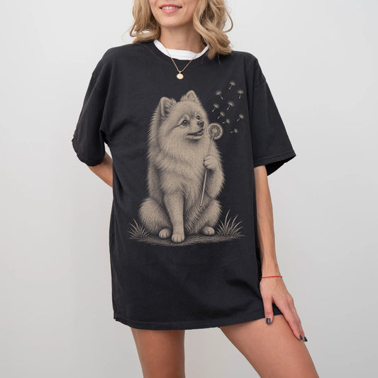 Model wearing a Black Comfort Colors® T-shirt showing Pomeranian portrait with drifting dandelion seeds
