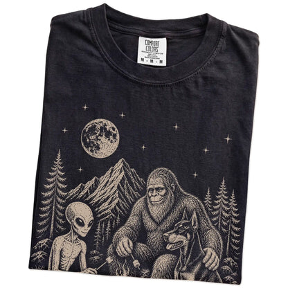 Folded Black Comfort Colors® T-shirt showing Doberman camping with Bigfoot and an alien