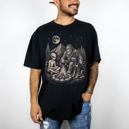 Model wearing a Black Comfort Colors® T-shirt showing Doberman camping with Bigfoot and an alien