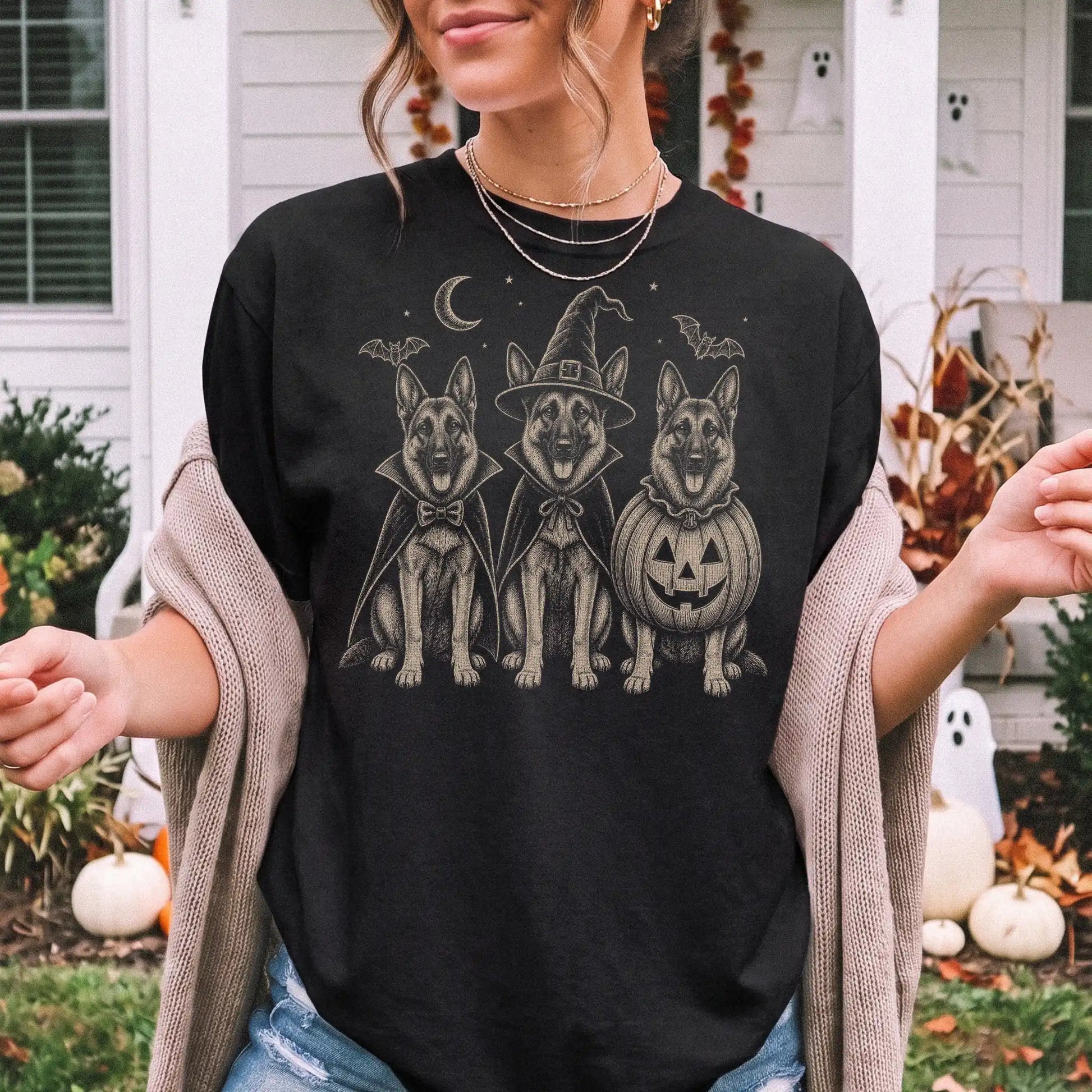 Model wearing a Black Comfort Colors® T-shirt showing three German Shepherd dogs dressed for Halloween beneath bats and a cre