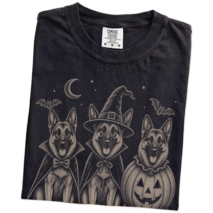 Folded Black Comfort Colors® T-shirt showing three German Shepherd dogs dressed for Halloween beneath bats and a crescent moo