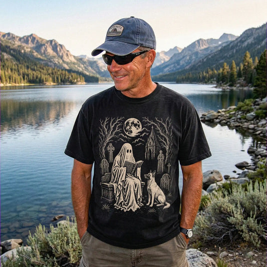 Model wearing a Black Comfort Colors® T-shirt showing Belgian Malinois beside a reading ghost in a moonlit graveyard