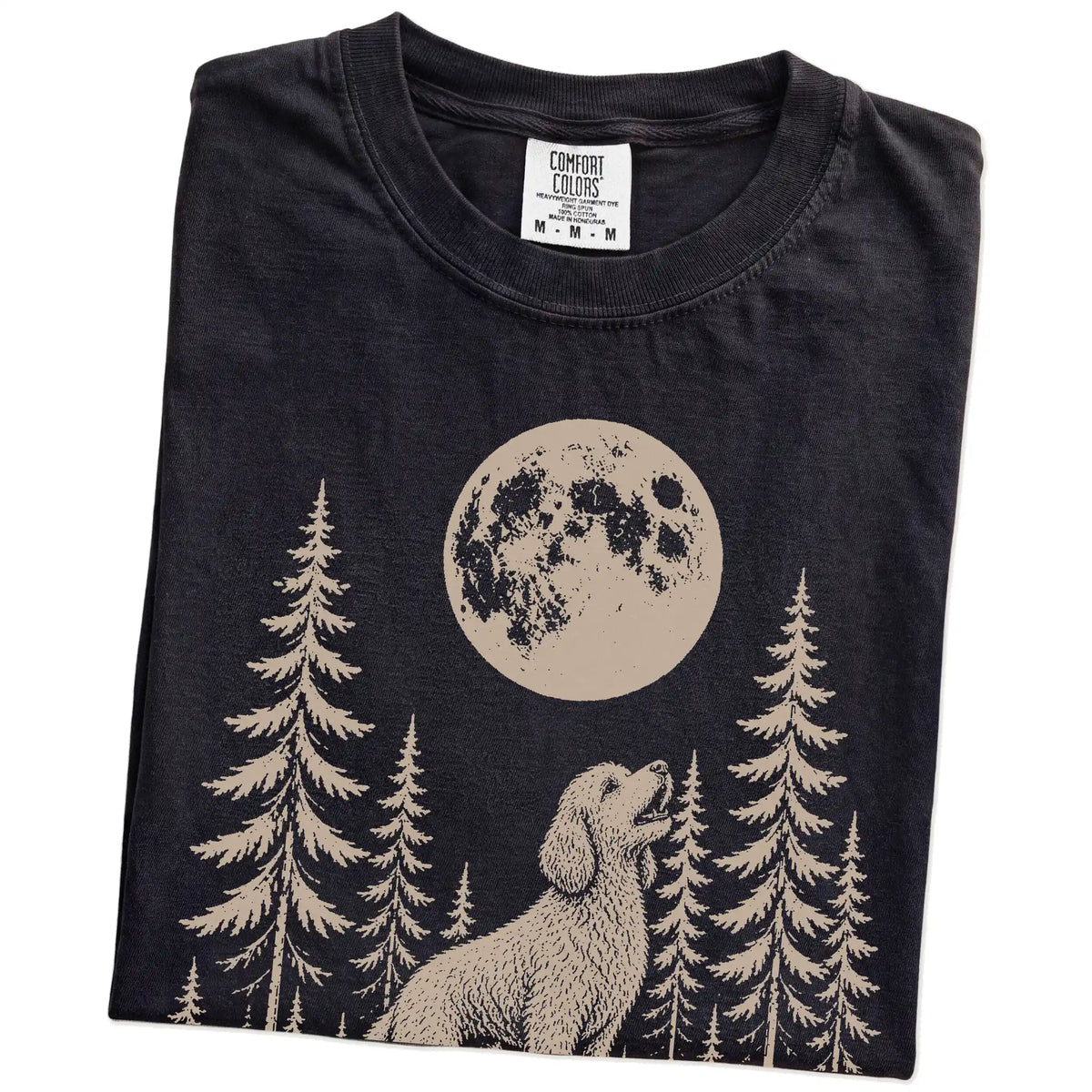 Folded Black Comfort Colors® T-shirt showing a Goldendoodle howling beneath the moon and pine trees