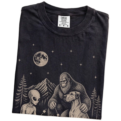 Folded Black Comfort Colors® T-shirt showing Great Dane camping with Bigfoot and an alien