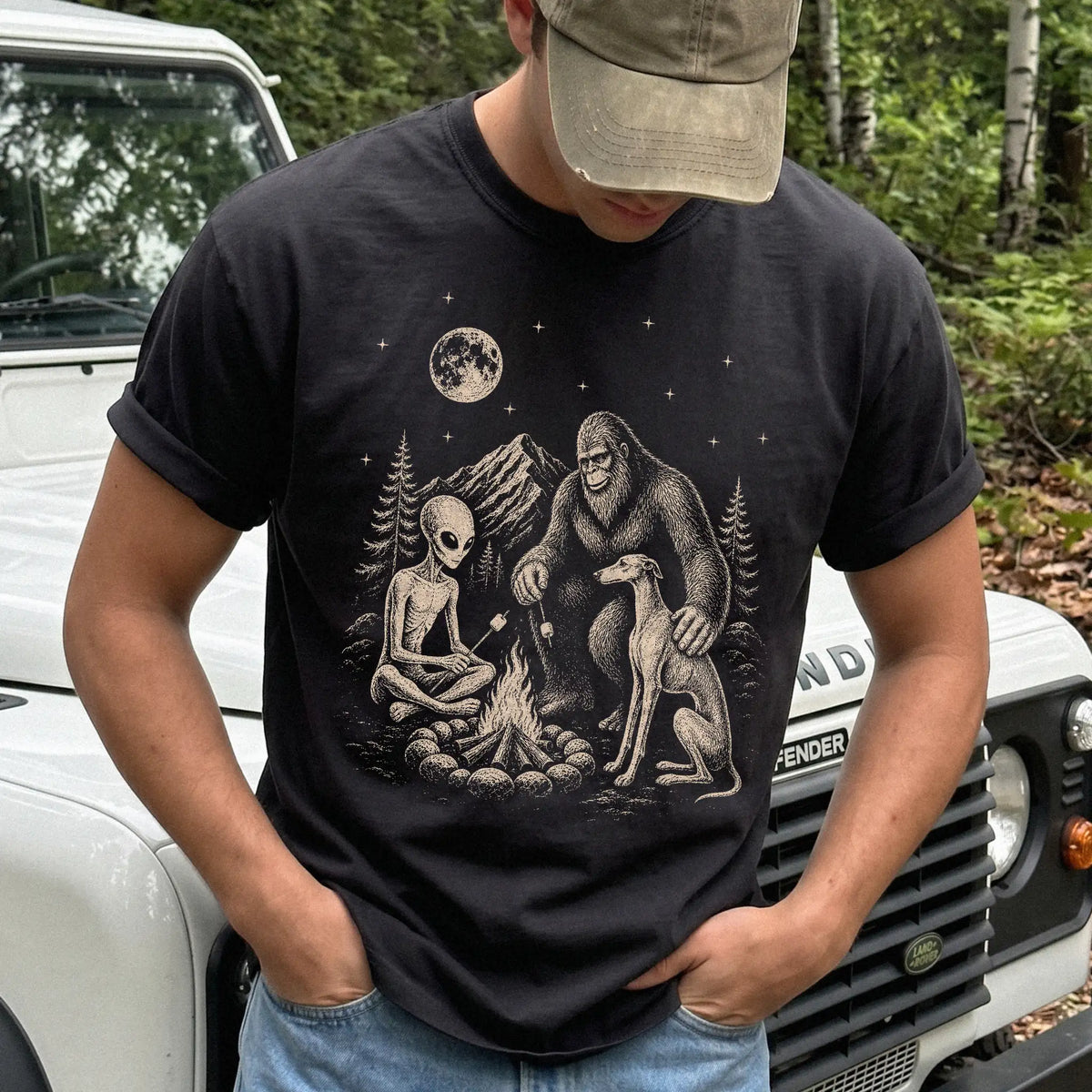 Model wearing a Black Comfort Colors® T-shirt showing Greyhound camping with Bigfoot and an alien