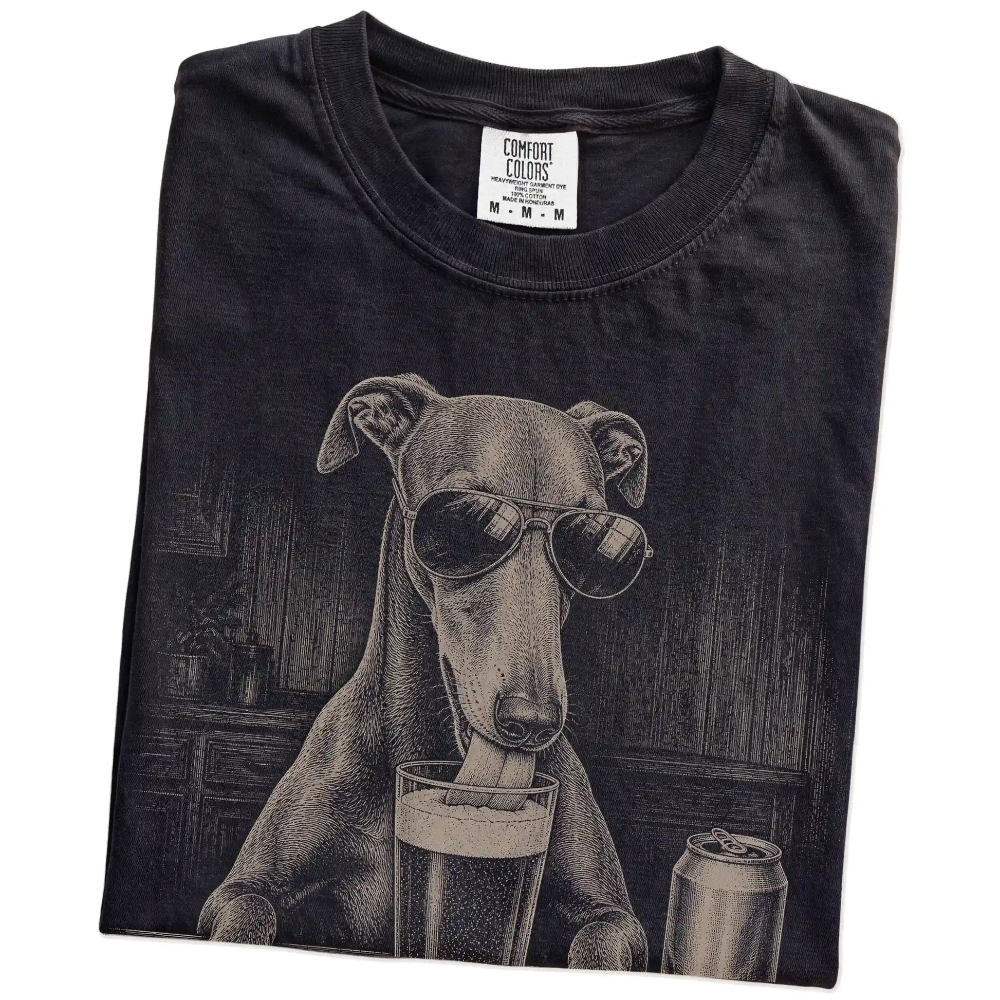 Folded Black Comfort Colors® t-shirt showing Greyhound sneaking a drink from a pint