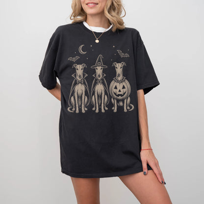 Model wearing a Black Comfort Colors® T-shirt showing three Greyhound dogs dressed for Halloween beneath bats and a crescent 