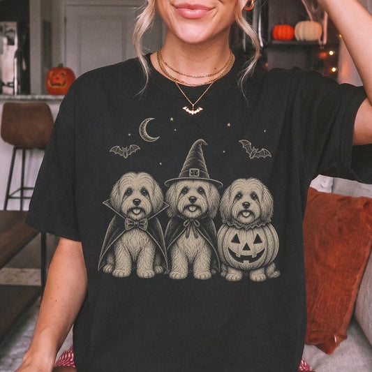 Model wearing a Black Comfort Colors® T-shirt showing three Havanese dogs dressed for Halloween beneath bats and a crescent m