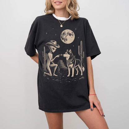 Model wearing a Black Comfort Colors® T-shirt with cowboy alien fist-bumping a husky beneath the moon